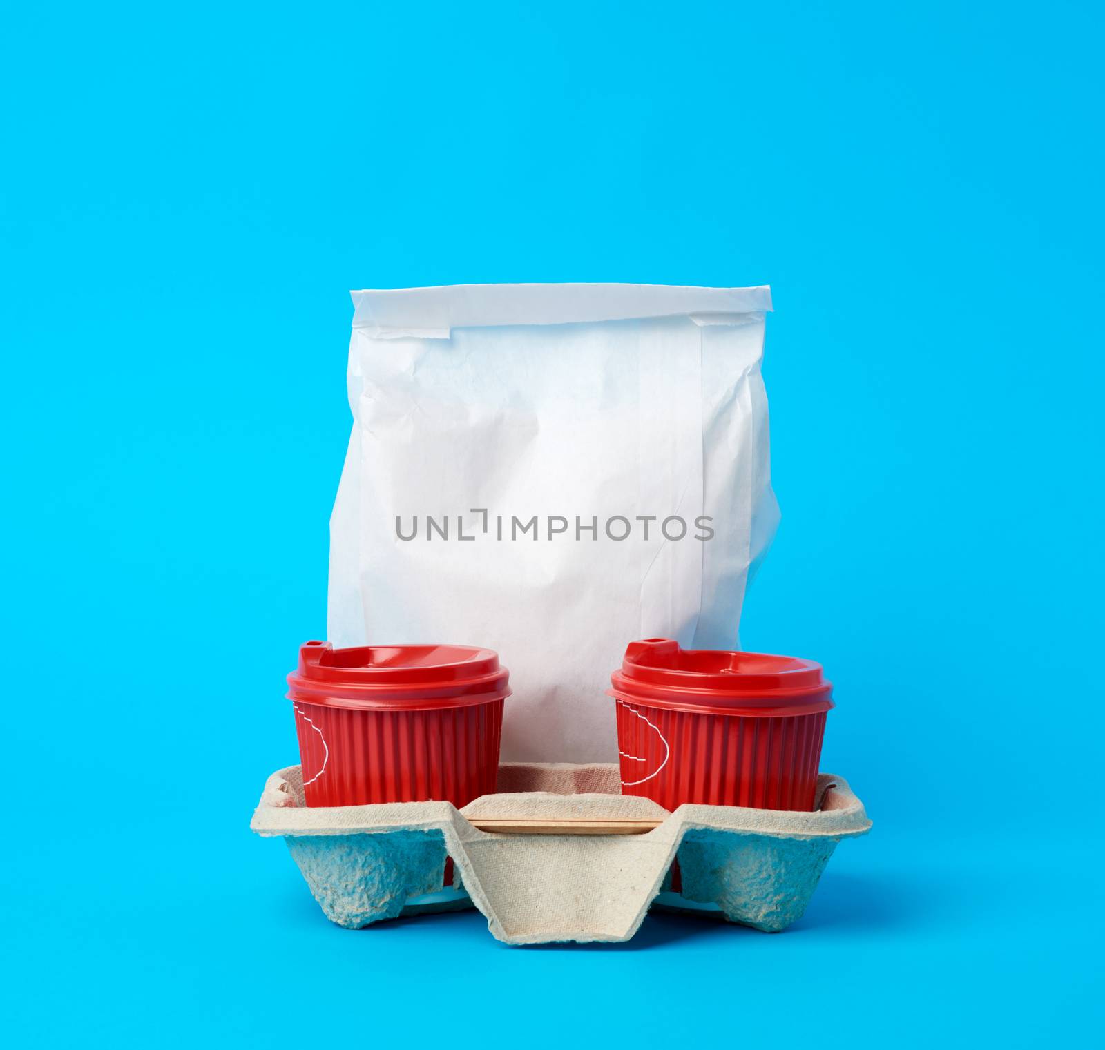 red disposable paper cups in the tray and a full white paper bag on a blue background, food delivery concept, order online