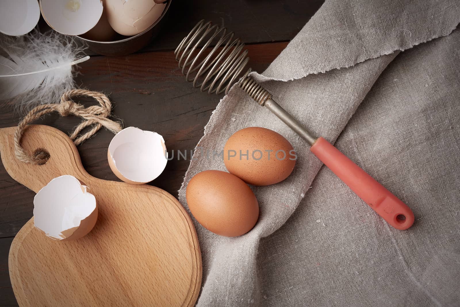 brown raw chicken eggs, shells, cutting board and hand-held whisk for protein on a wooden table, top view
