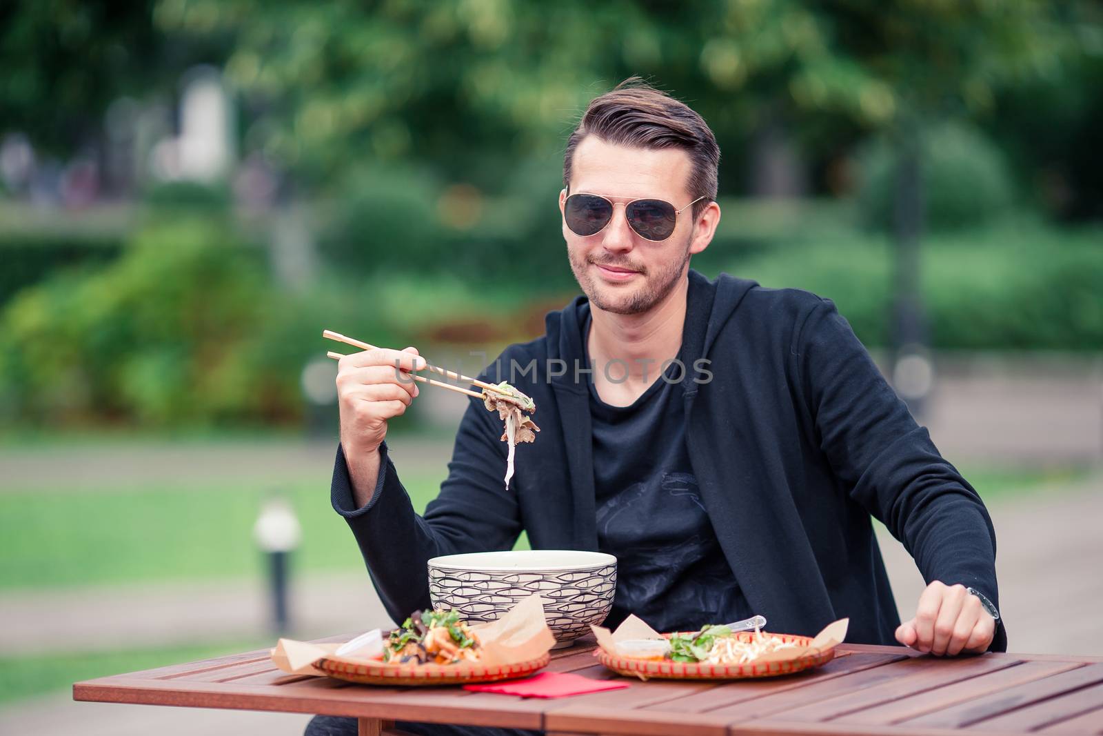 Young man eating take away noodles on the street by travnikovstudio