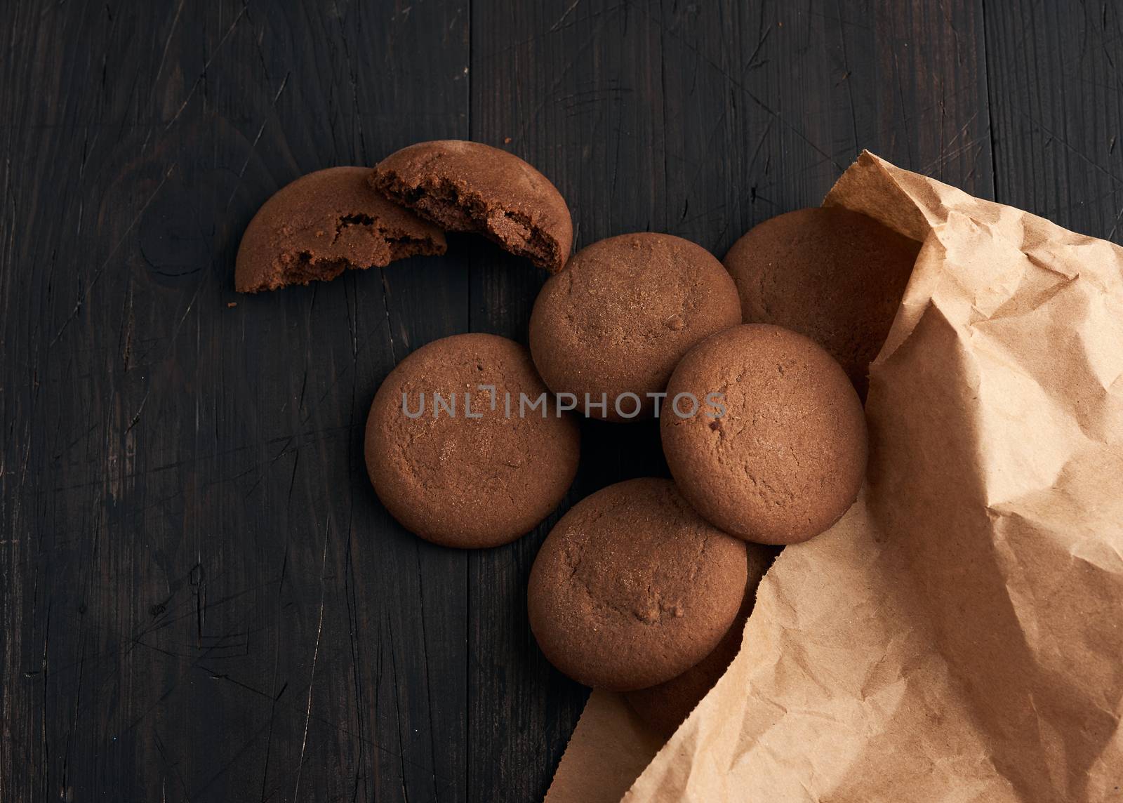 round chocolate chip cookies lie on a brown wooden table, dessert spilled out of a paper bag, top view