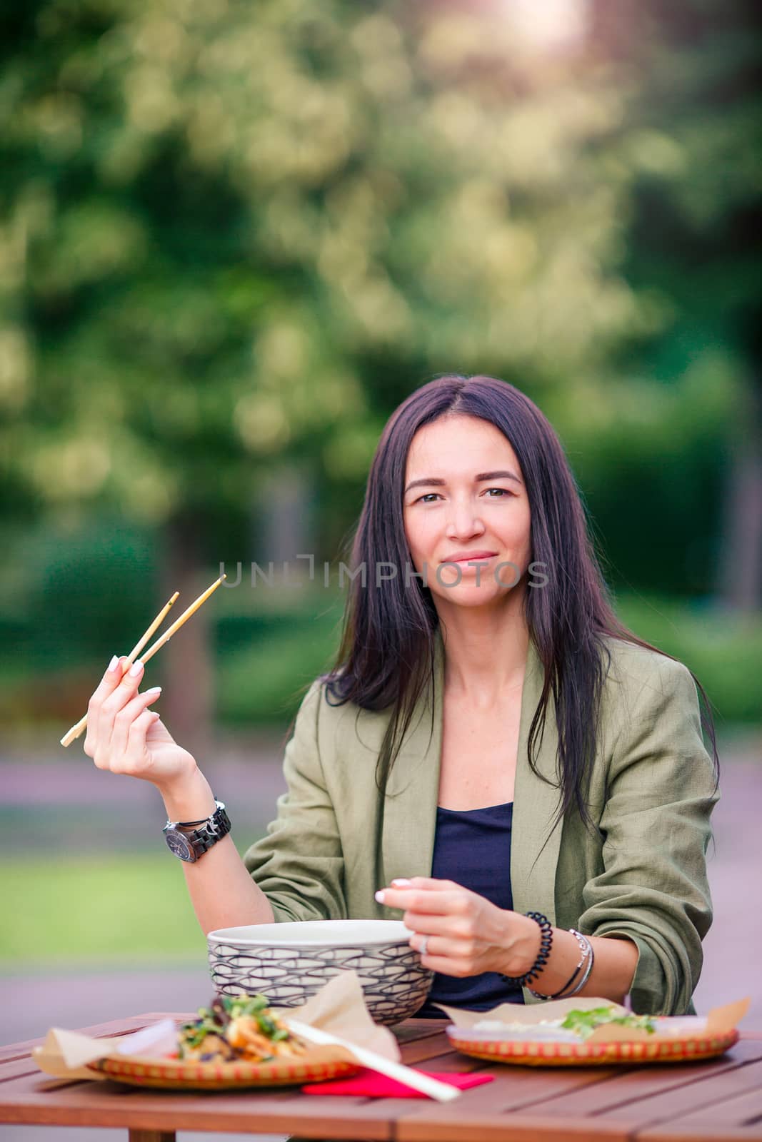 Young woman eating take away noodles on the street by travnikovstudio