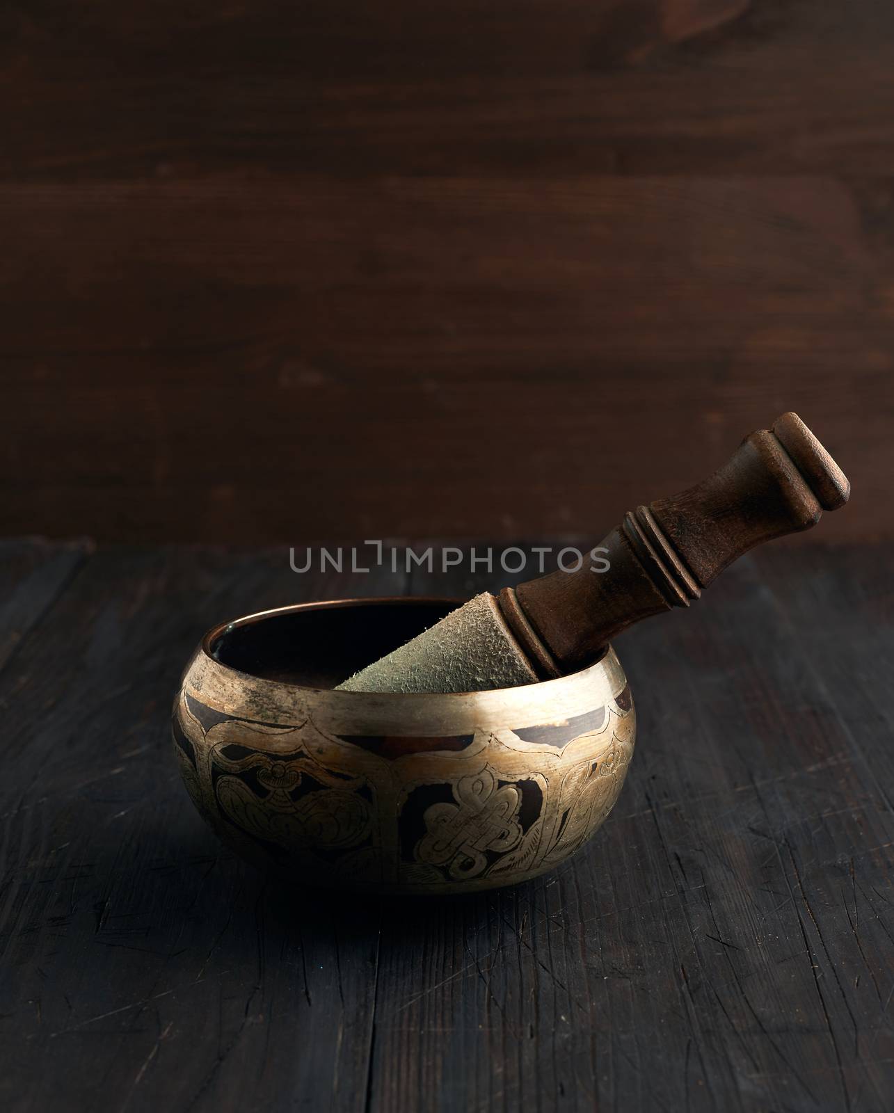 Tibetan singing copper bowl with a wooden clapper on a brown woo by ndanko