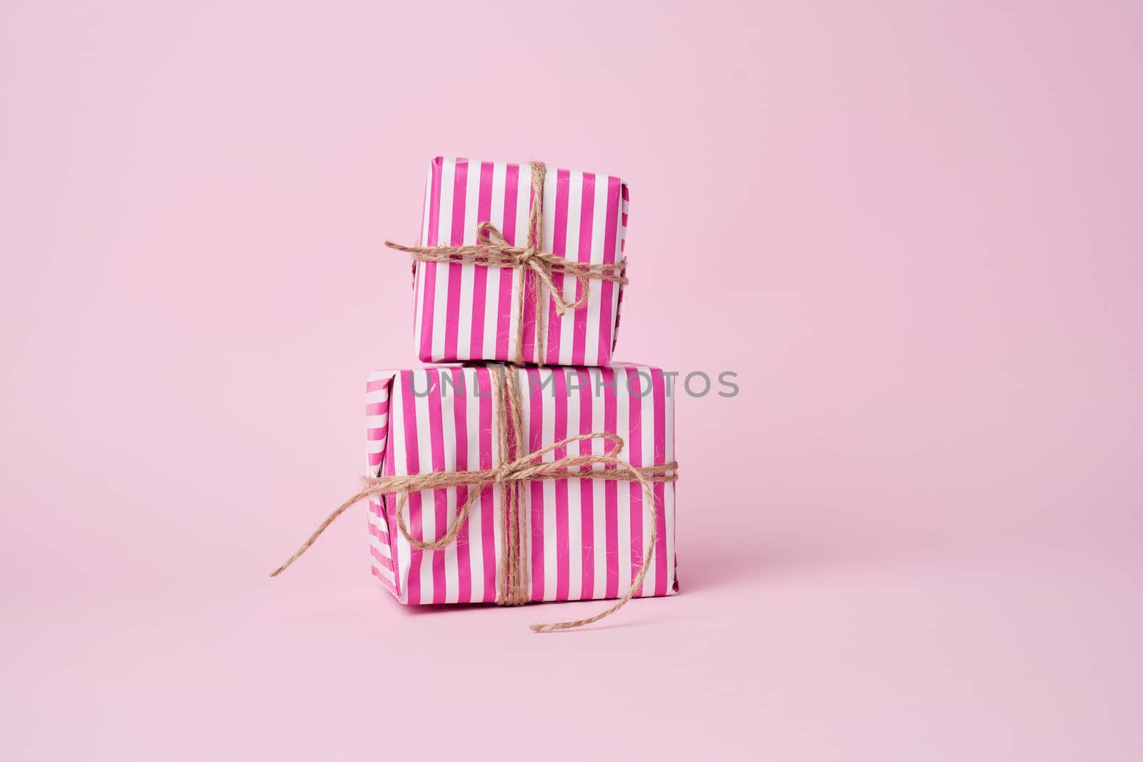 two boxes wrapped in pink paper and tied with a brown rope on a pink background, holiday backdrop 