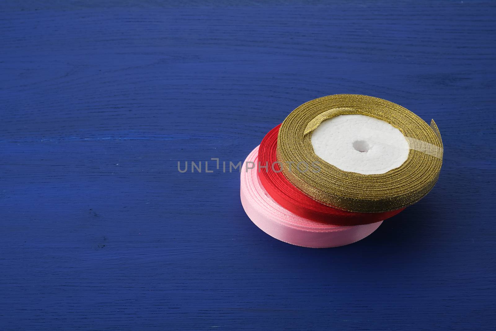 round bobbins with red, pink,  golden ribbon on a blue wooden background, top view