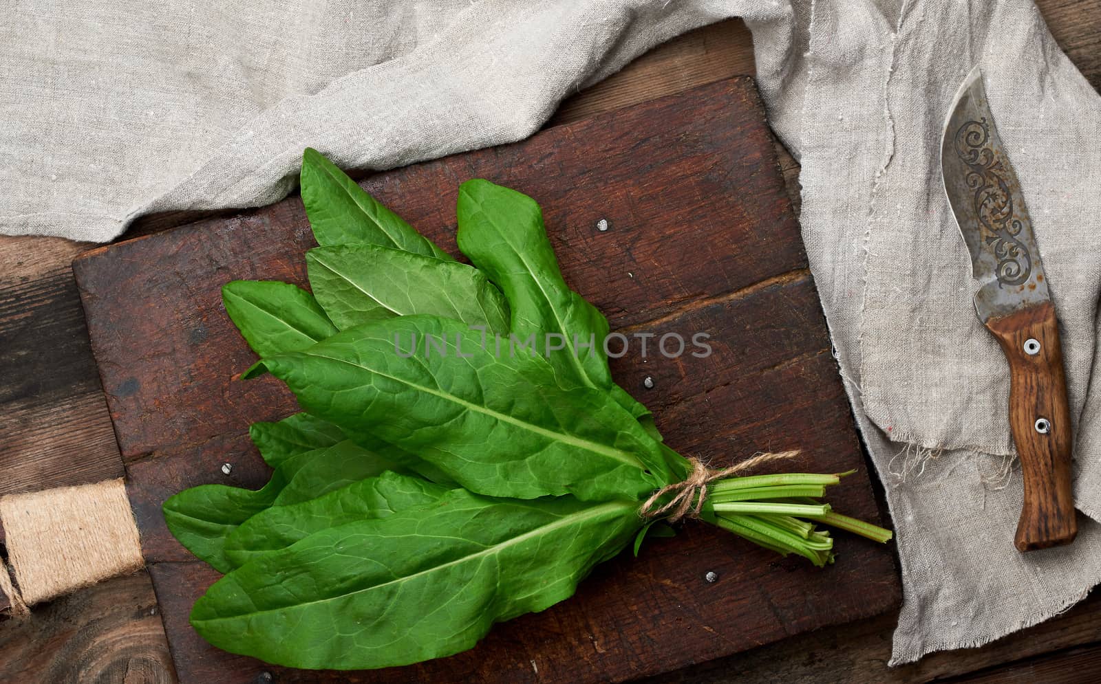 bunch of fresh green sorrel leaves and old brown cutting board on a wooden table, top view