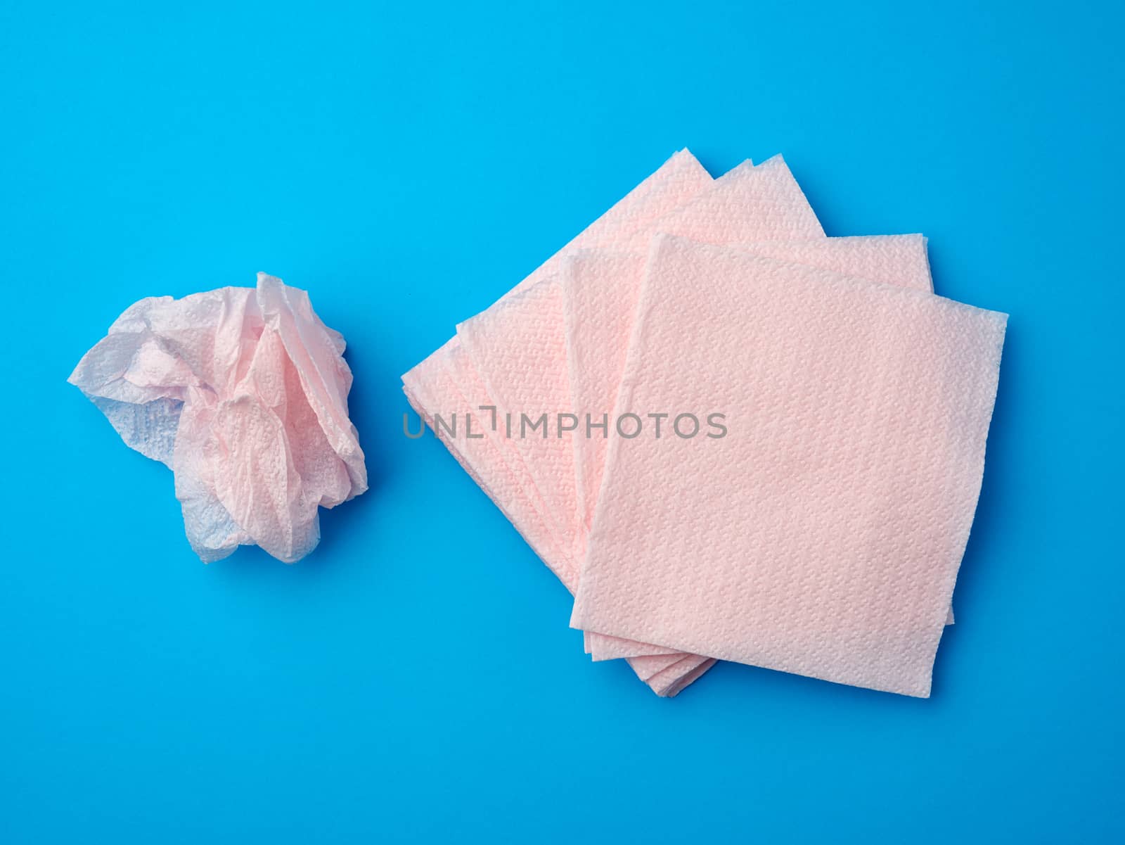 crumpled pink paper disposable napkins on a blue background, top view