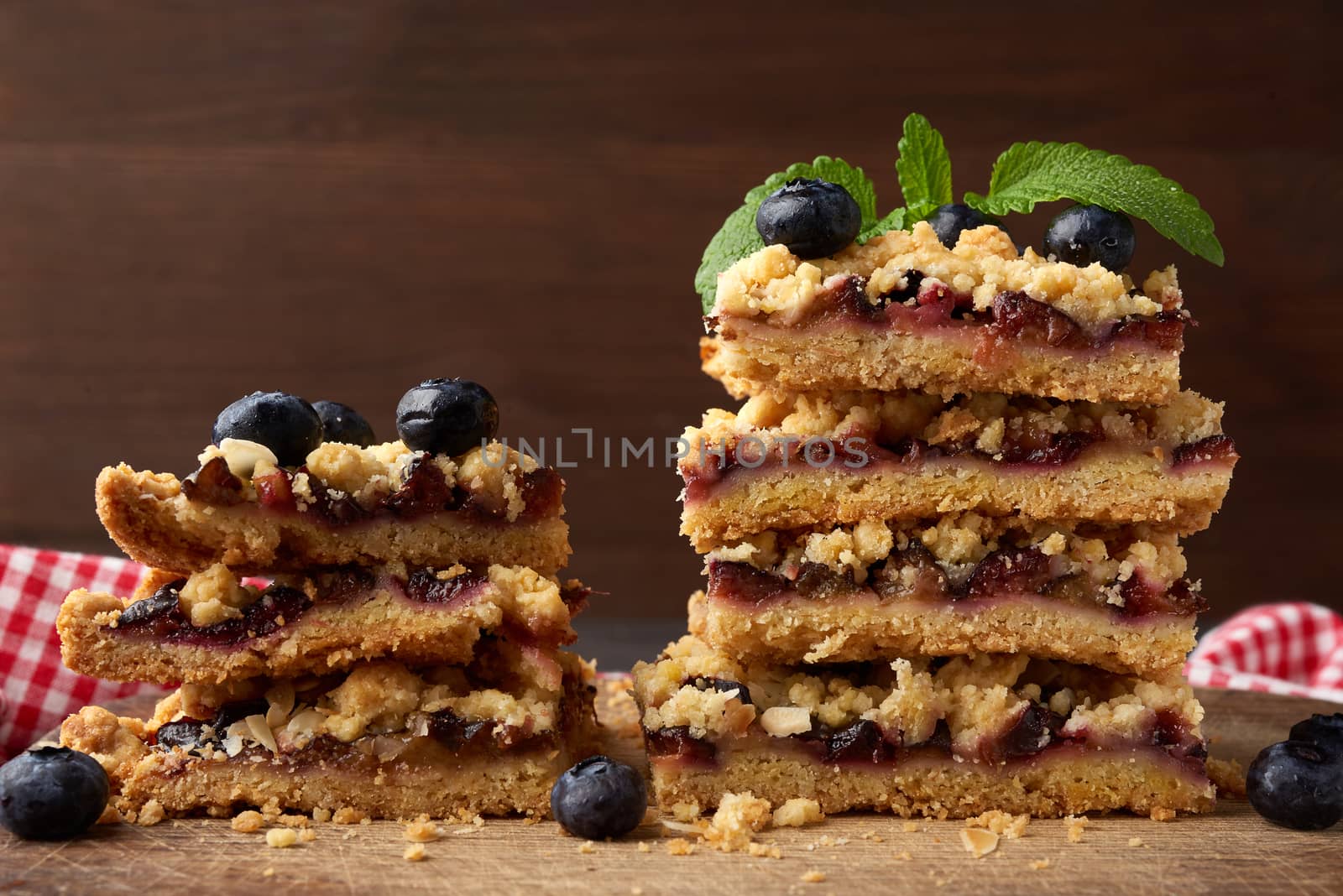 stack of square slices of baked crumble pie with blue plum on a wooden board, delicious dessert