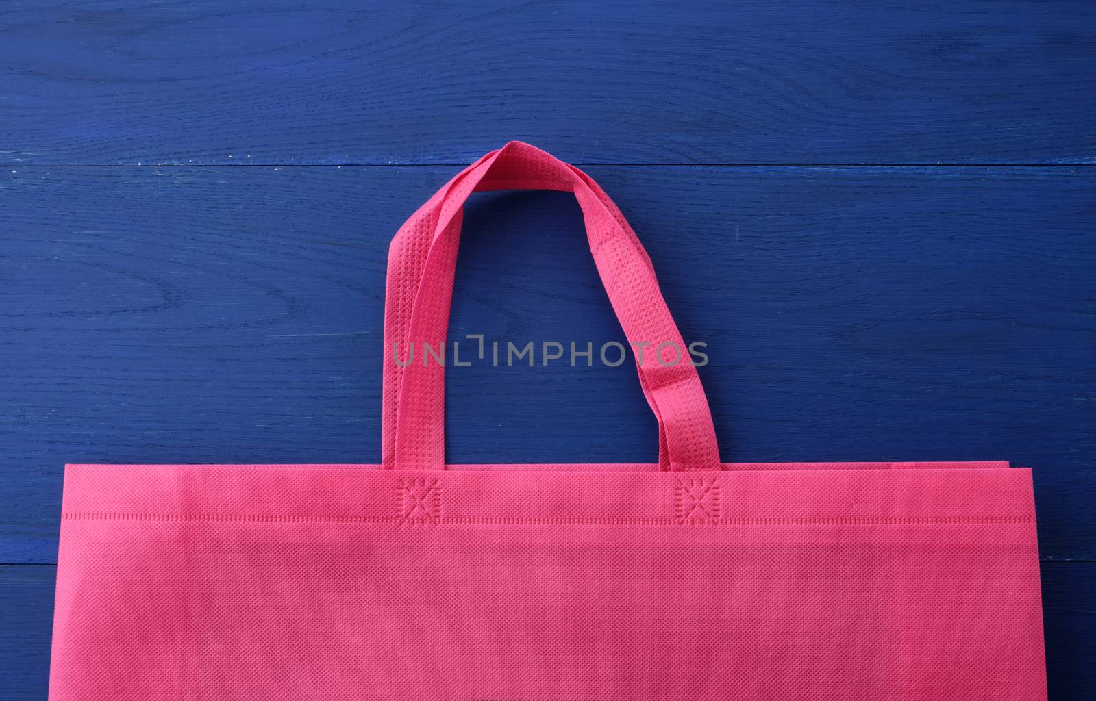 Reusable pink viscose bag on blue wooden background, plastic waste reduction concept
