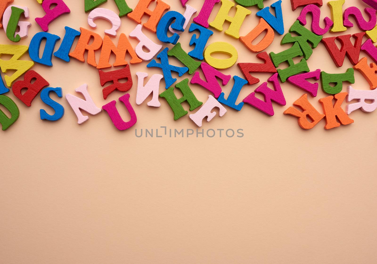 multi-colored wooden letters of the English alphabet on a beige background, top view, copy space