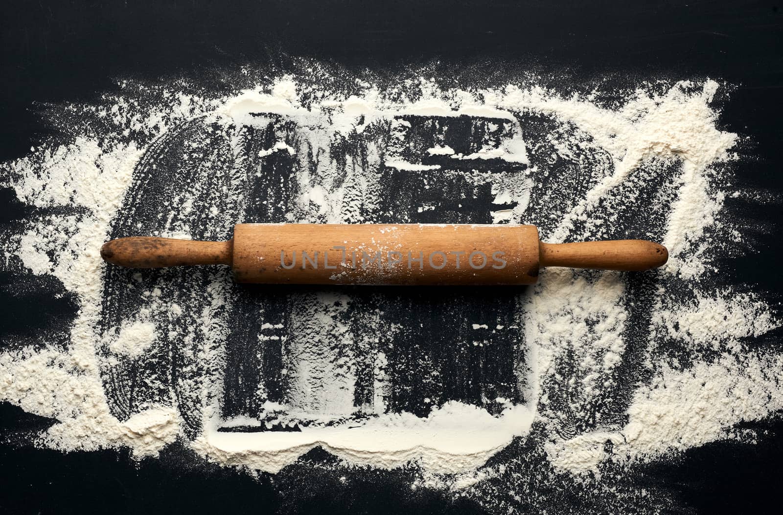 white wheat flour scattered on a black table and a wooden rolling pin on a black table, top view, place for an inscription
