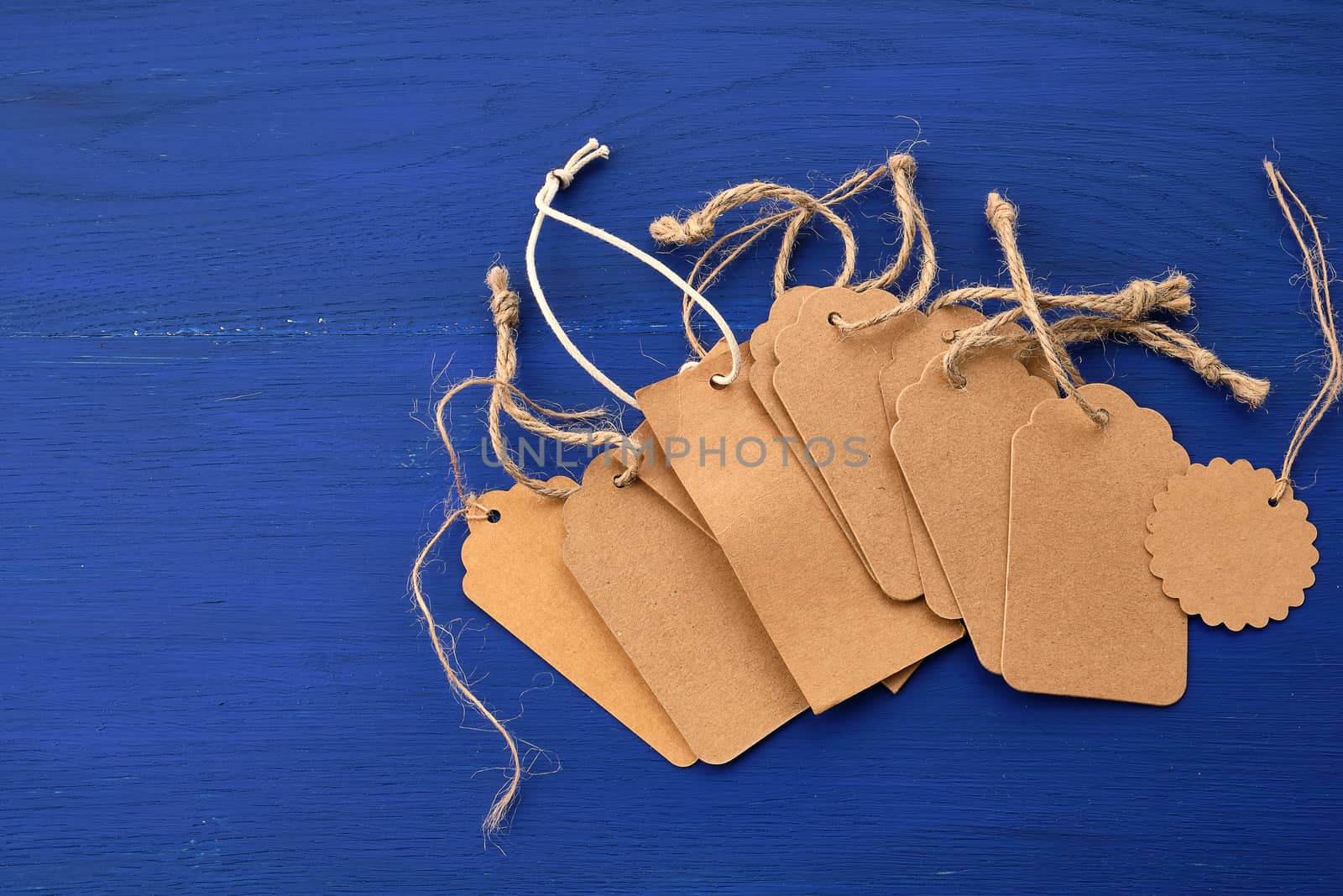 stack of empty brown empty tags from kraft paper with ropes for clothes and other purposes on a blue wooden background. Design element.