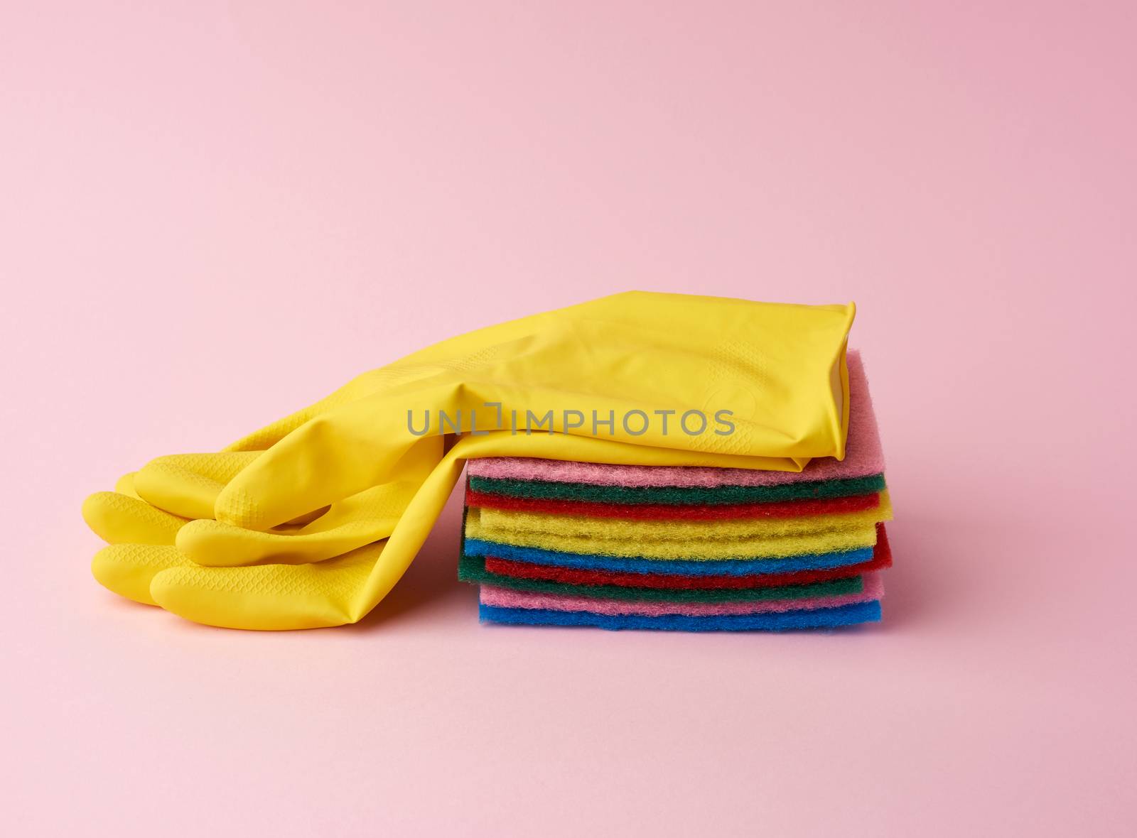 multi-colored kitchen sponge, rubber yellow gloves on a pink background, set of items for cleaning