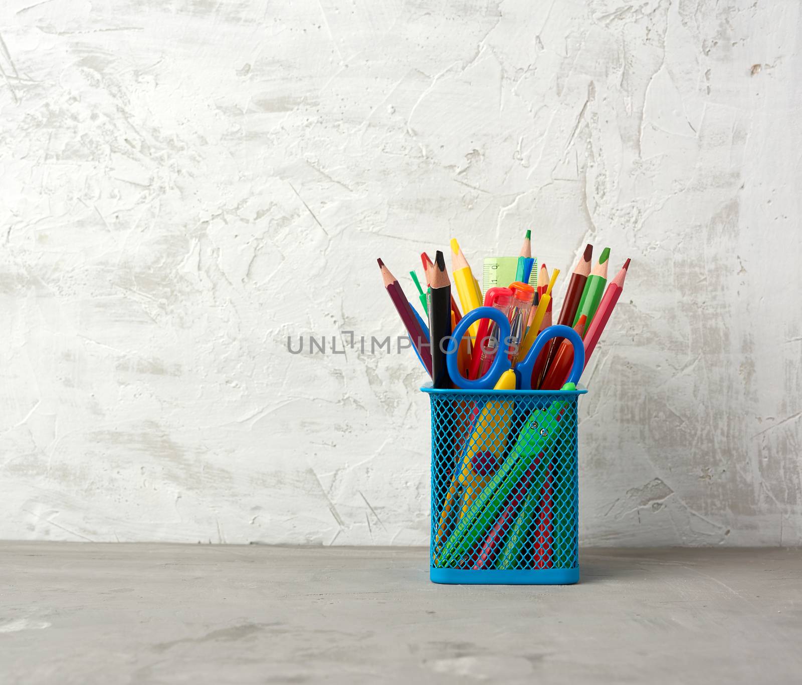 multicolored pens and pencils and other stationery in a blue metal holder, gray background