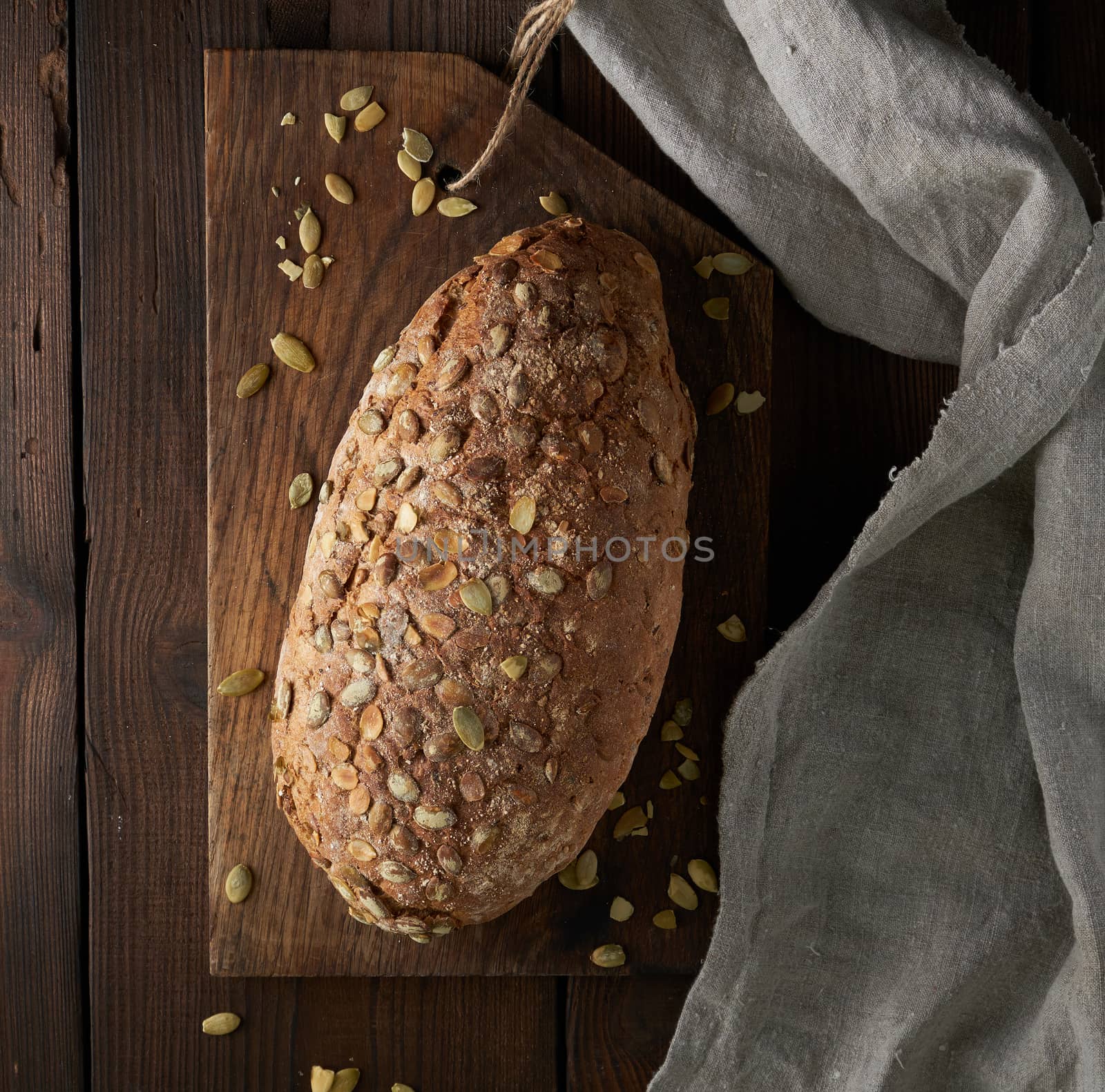 baked oval bread made from rye flour with pumpkin seeds on a gray linen napkin, top view