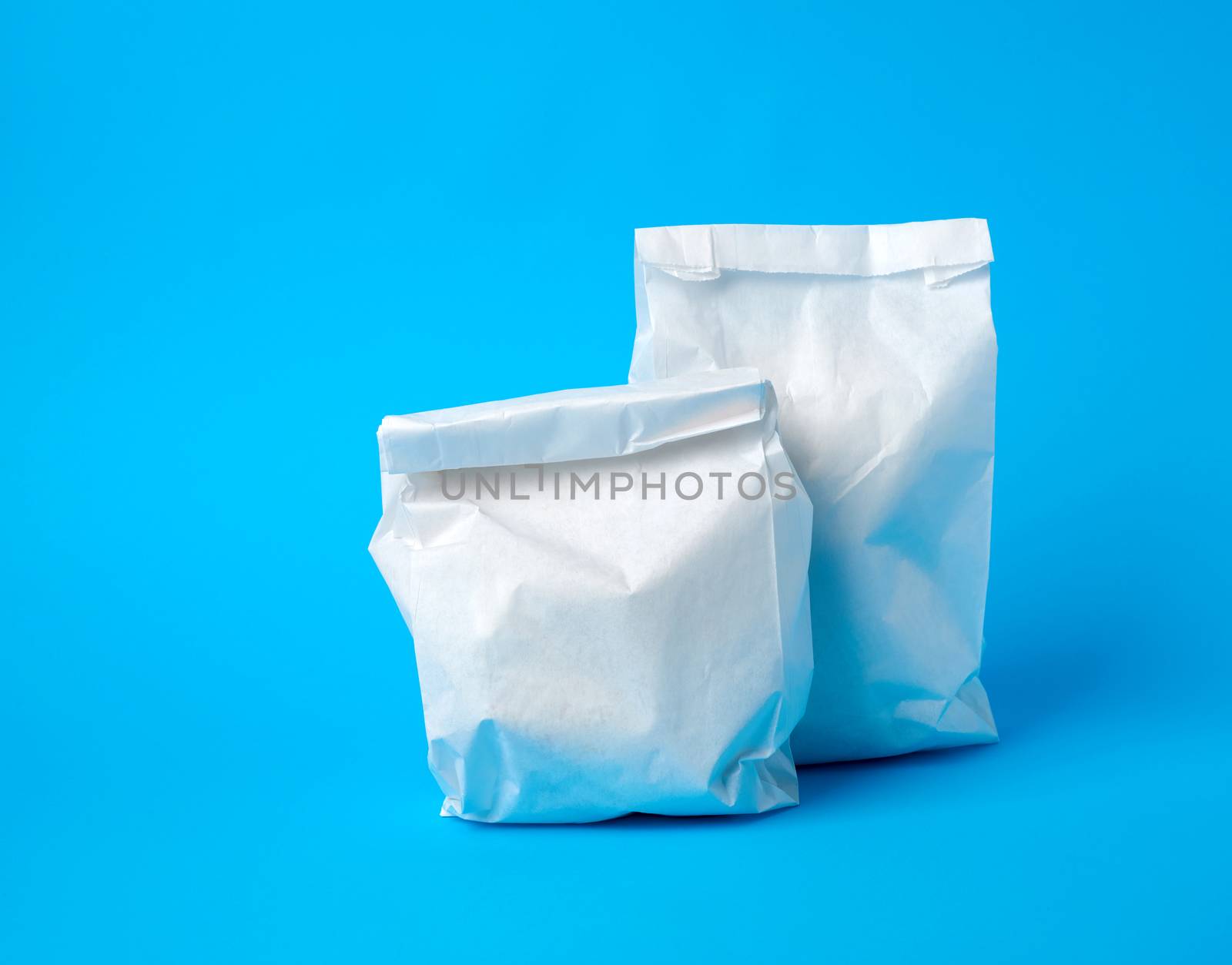 two full paper disposable food bags on a blue background, concept of delivery and ordering food