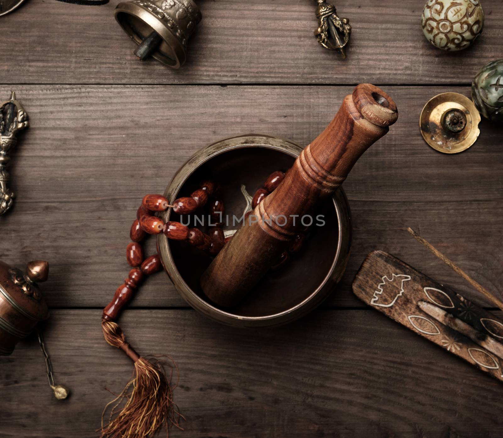 Copper singing bowl, prayer beads, prayer drum and other Tibetan religious objects for meditation and alternative medicine on a brown wooden background