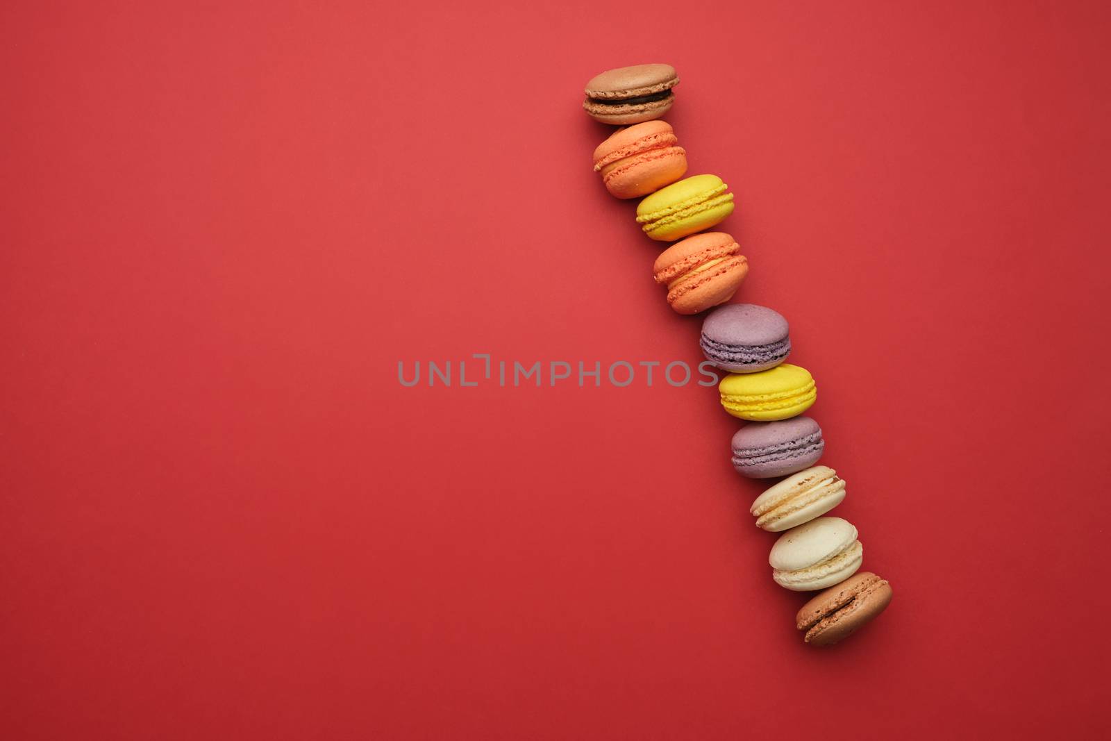round multi-colored baked macarons with cream lie in a line on a red background, flat lay, copy space 