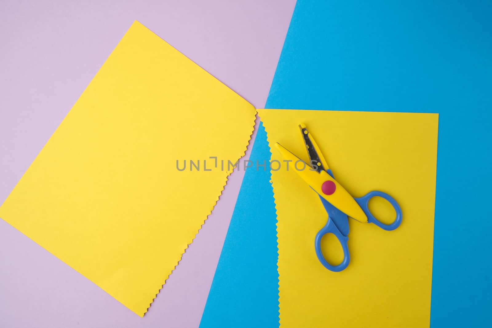 abstract background of colored paper, yellow stripes with a zigzag end and plastic scissors, top view