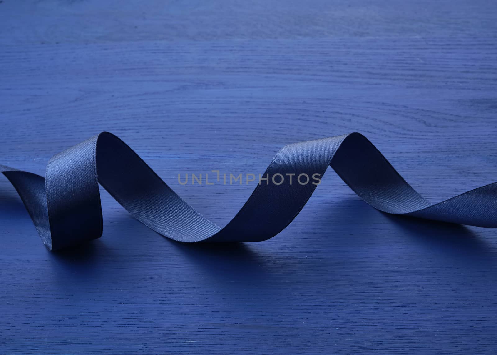 dark blue silk thin ribbon twisted on a blue wooden background, trendy classic color, top view