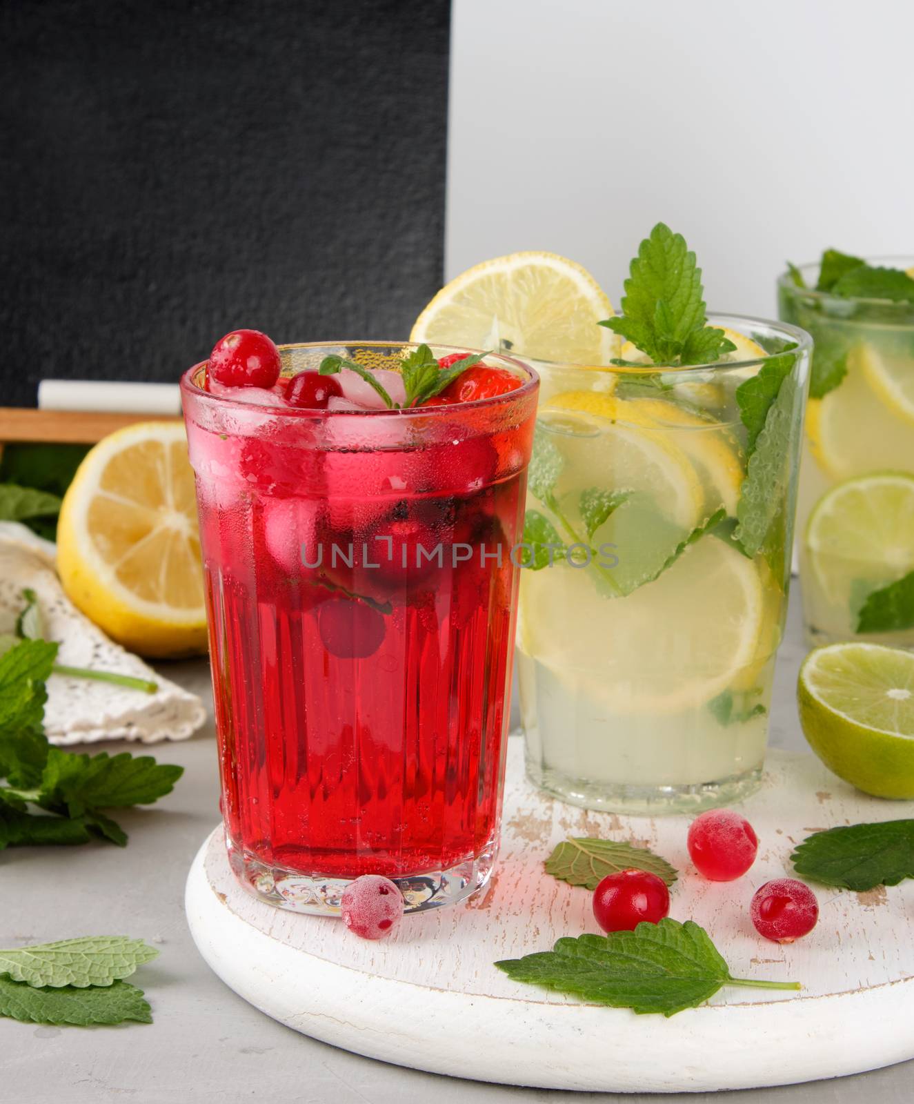 refreshing summer drink of strawberries and cranberries on a white wooden board, behind it are yellow lemons and green mint leaves