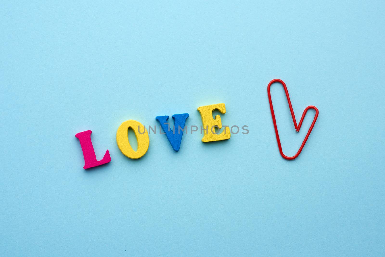 word love made of multi-colored wooden letters and a red paper clip in the shape of a heart on a blue background, top view