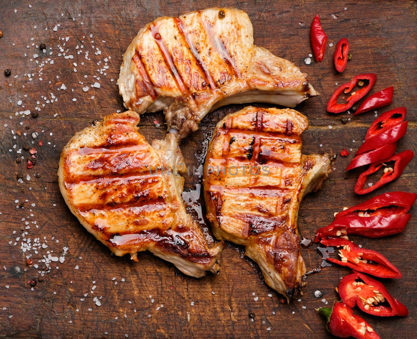 pork fried steak on the rib lies on a vintage brown wooden board, next to fresh red chili peppers, top view