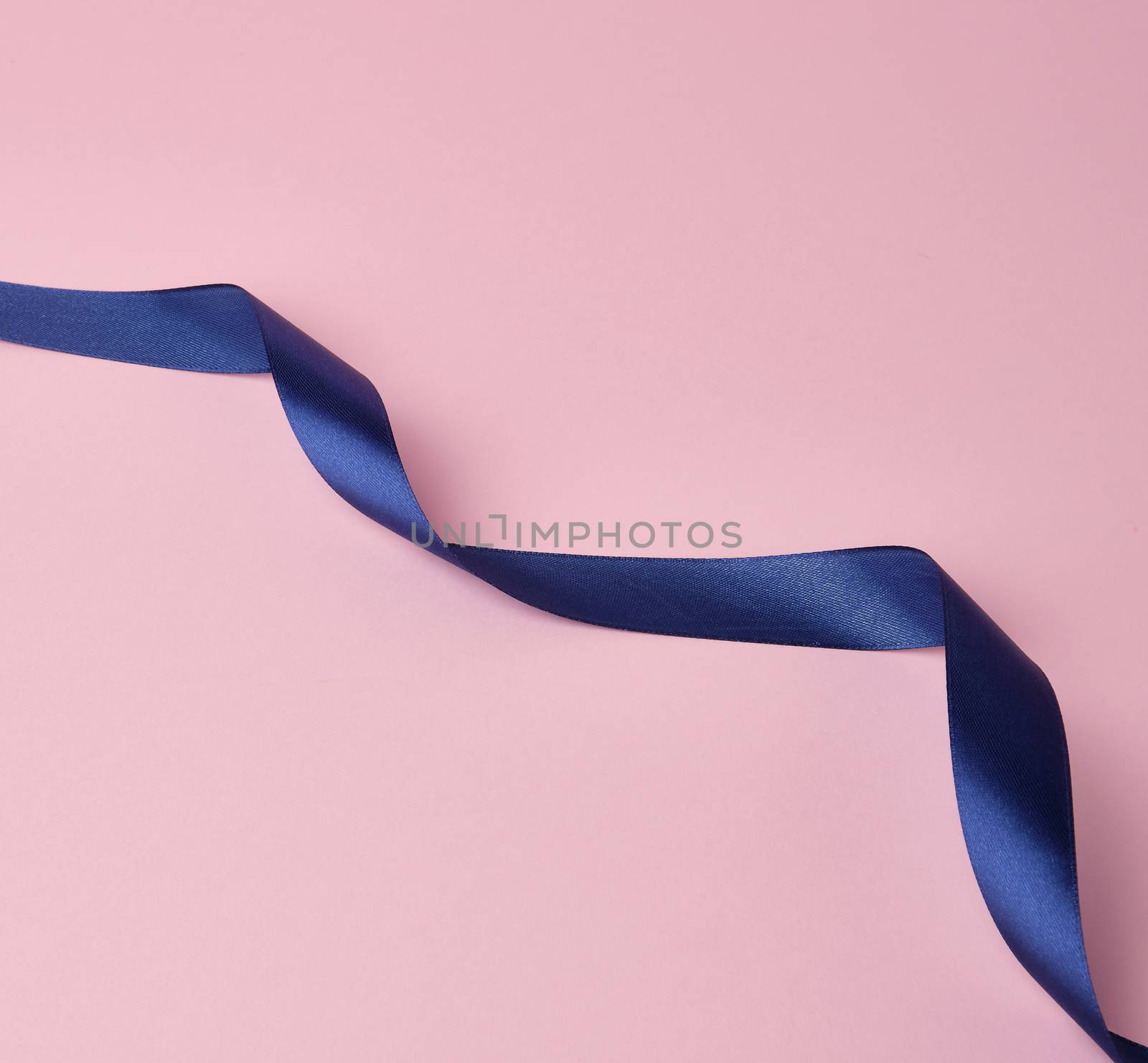 dark blue silk ribbon twisted into loops on a pink background, abstract background for the designer