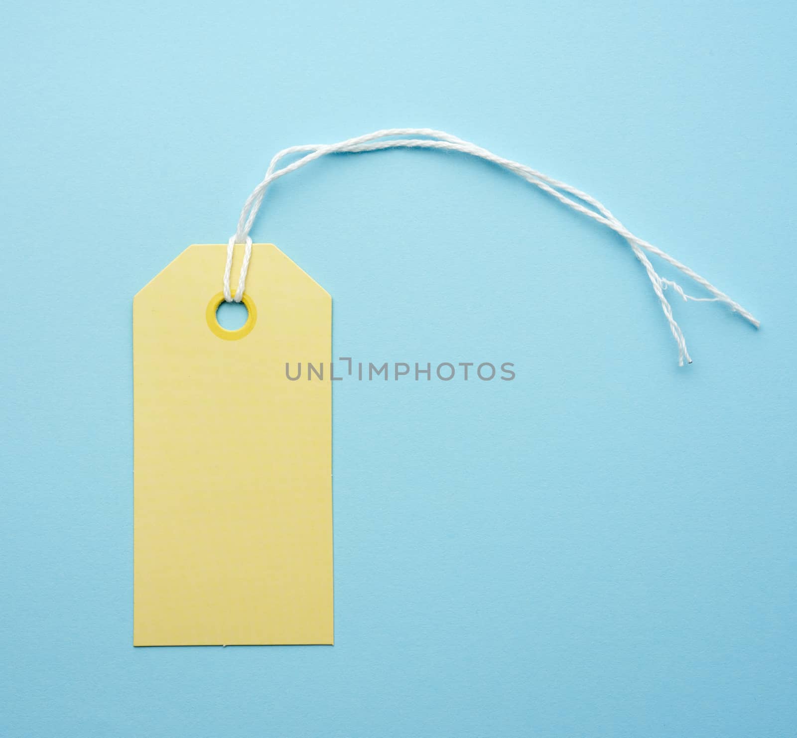 empty yellow paper tag tied with white string. Price, gift, sale tag on the blue background, close up