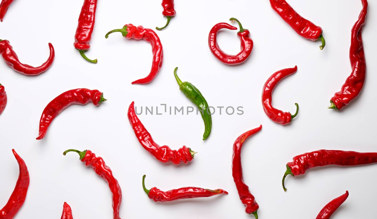 many red whole fruits of hot pepper and one green on a white background, concept of difference and discrimination