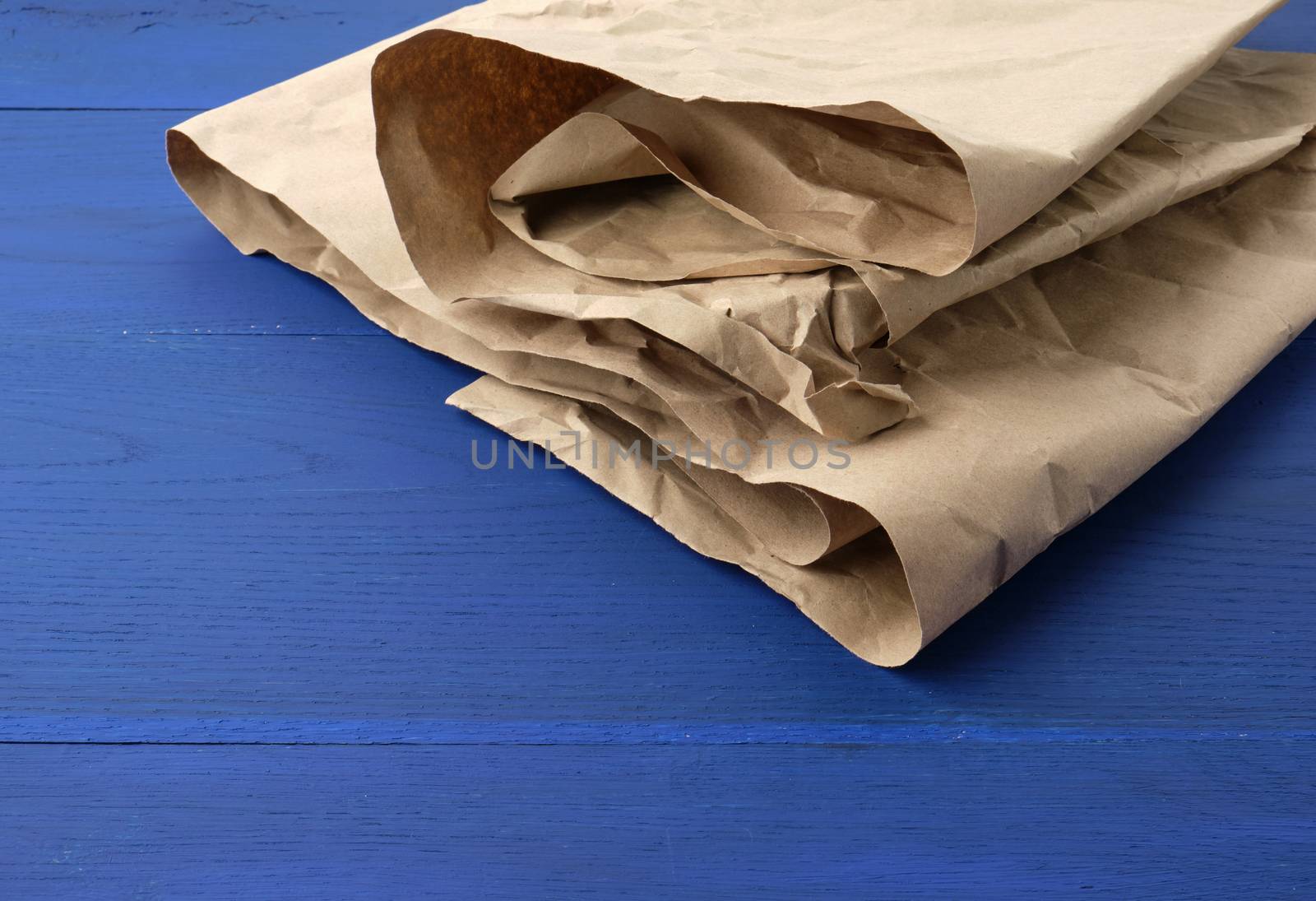 brown crumpled kraft paper sheet on blue wooden background, close up