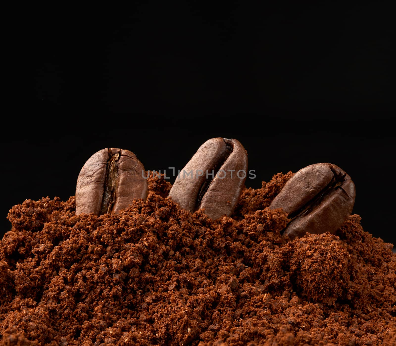 pile of ground roasted coffee arabica and whole grains on a black background, ingredient for a fragrant drink