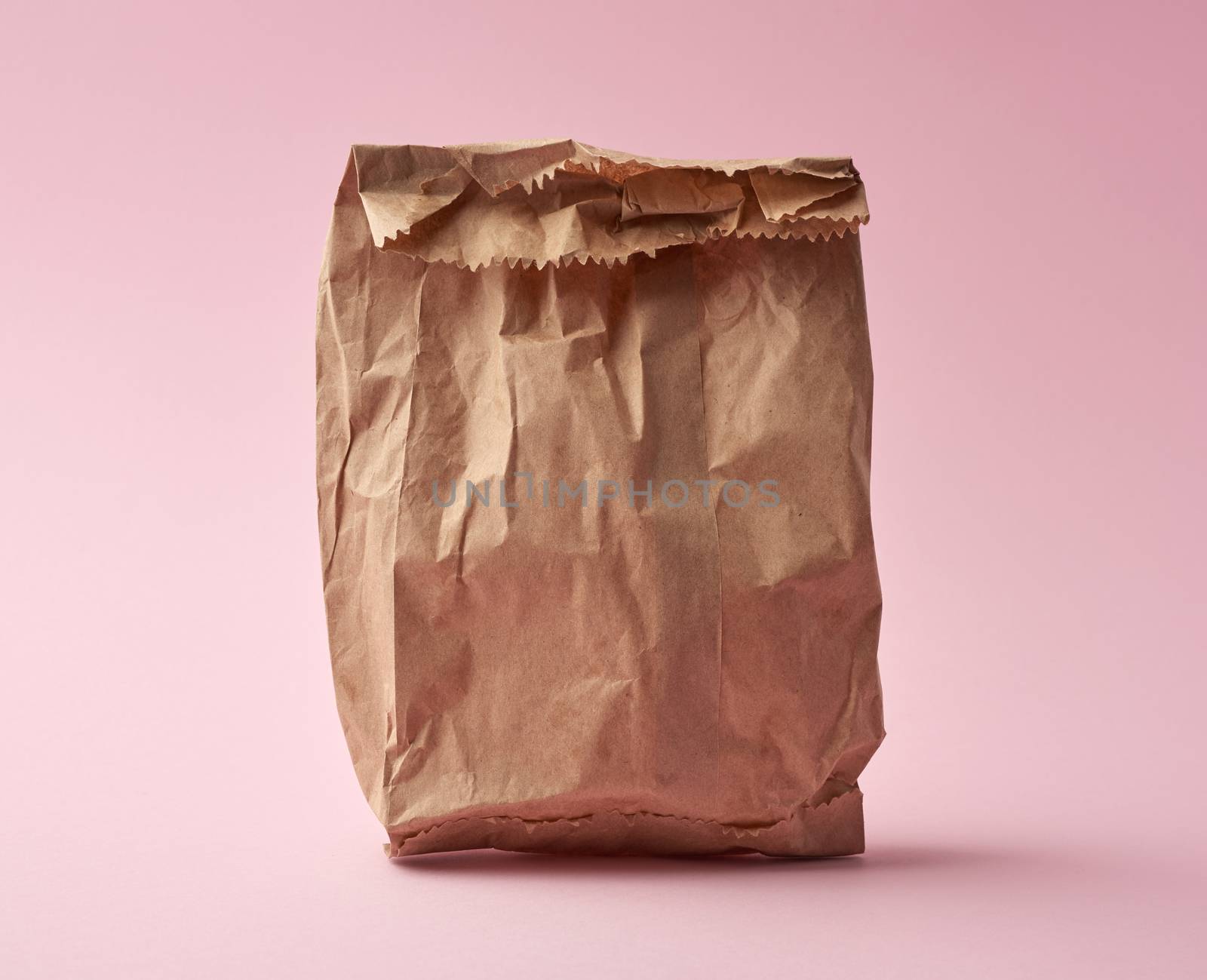 full paper disposable bag of brown kraft paper on a pink background, concept of rejection of plastic packaging, template for designer, packaging for contactless product delivery