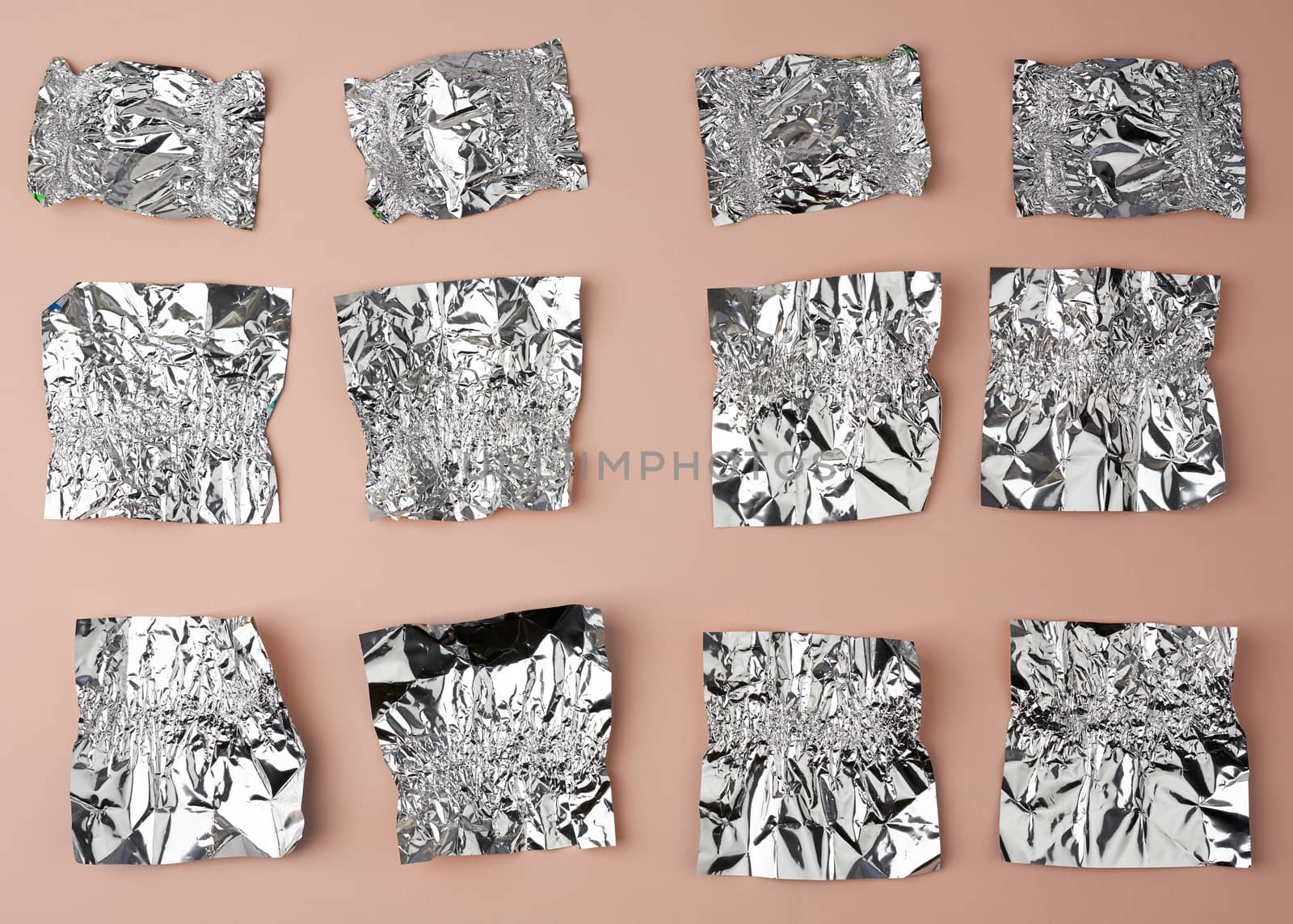 various crumpled foil used candy wrappers on a beige background, top view