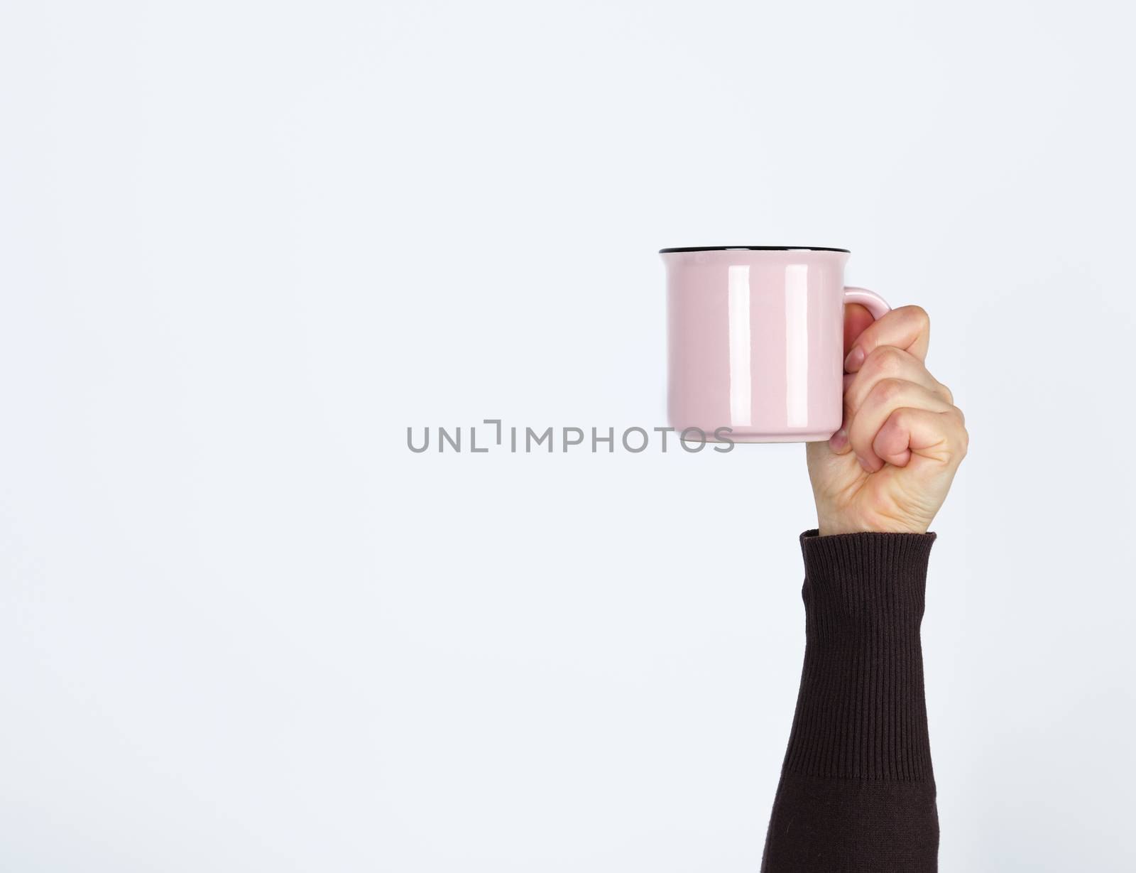 pink ceramic cup in a female hand on a white background, hand is raised up