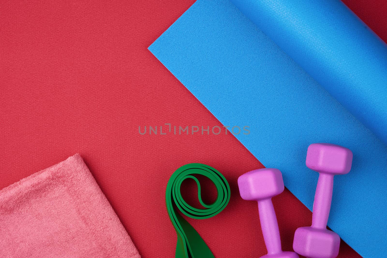 pair of purple plastic dumbbells, green elastic and pink terry towel on a blue neoprene mat, top view, training equipment