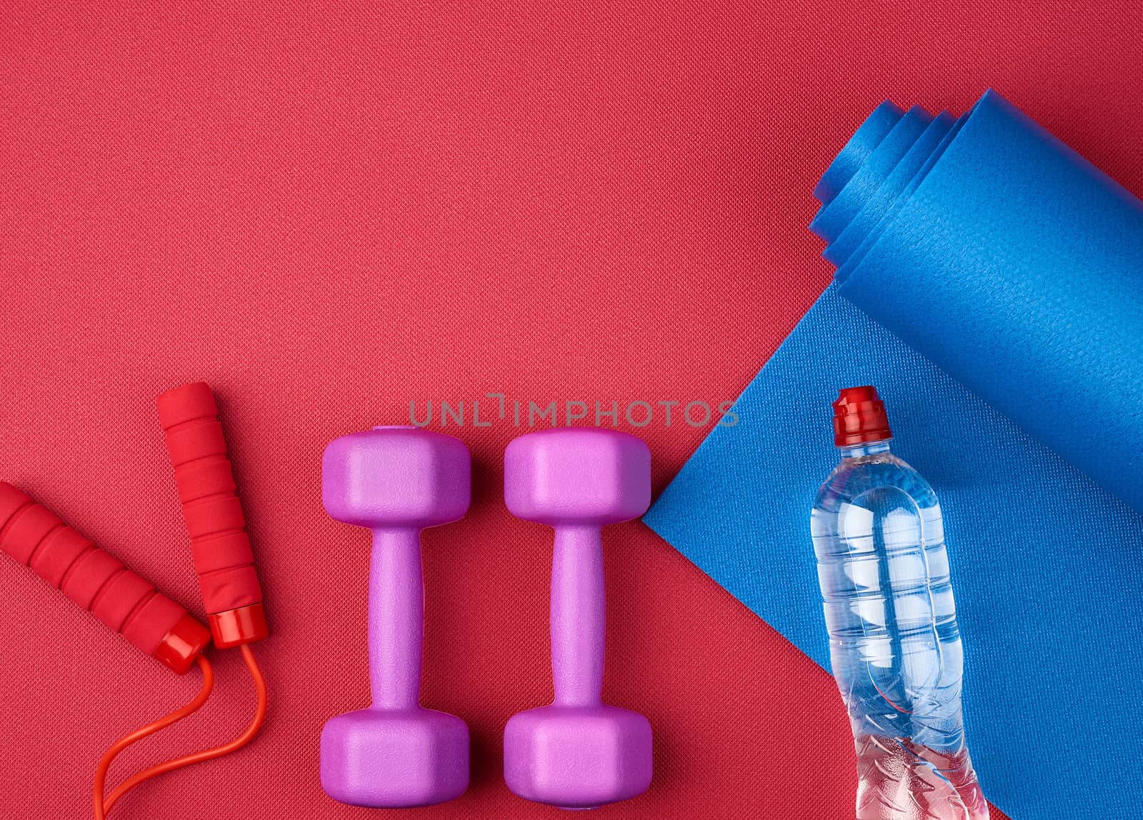 pair of purple plastic dumbbells, bottle of water  on a red neoprene mat, top view, training equipment