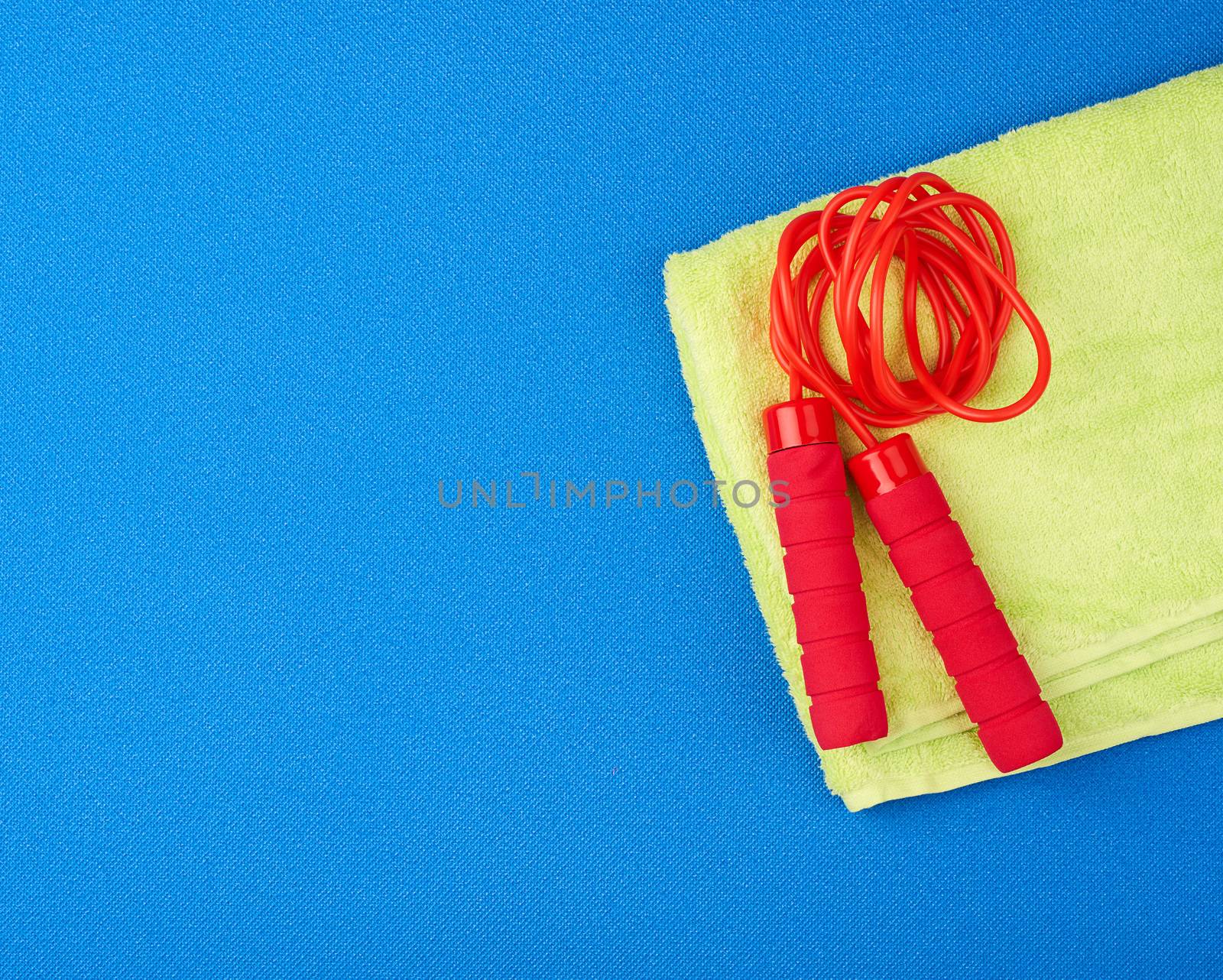 red jump rope lies on a neoprene blue sports mat and green towel, copy space