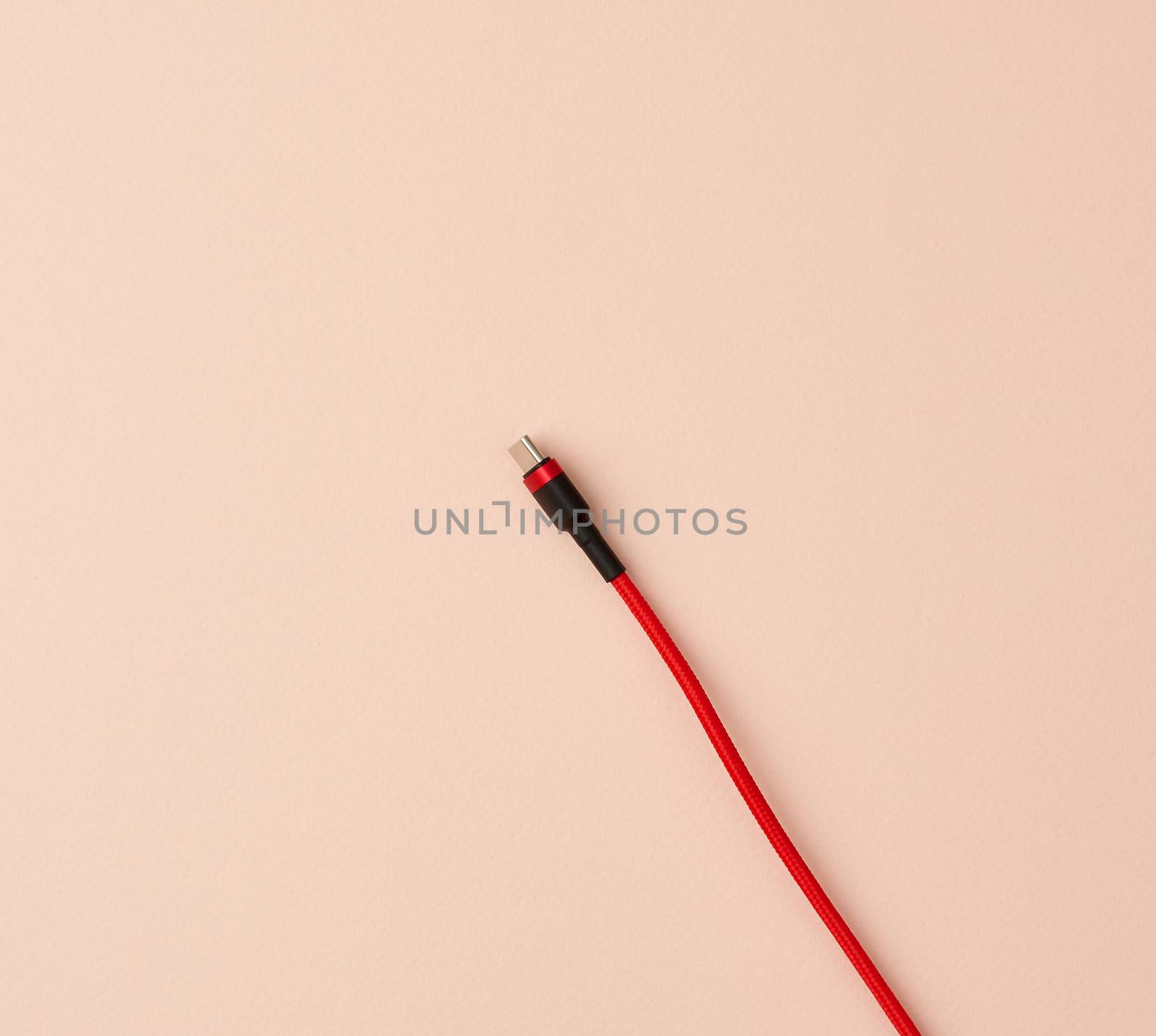 micro cable for charging mobile devices in a red textile braid on a beige background