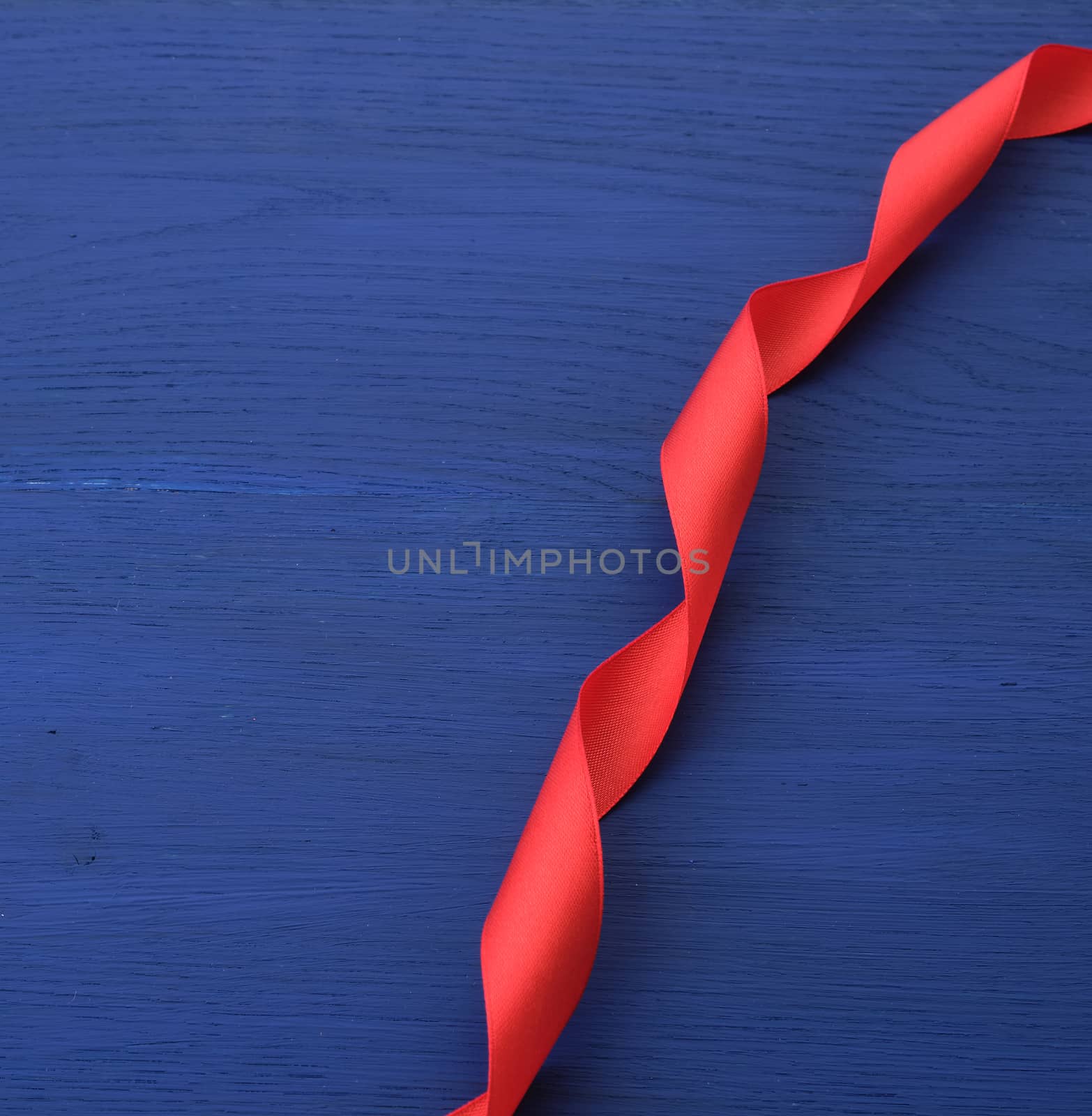 red silk thin ribbon twisted on a blue wooden background by ndanko
