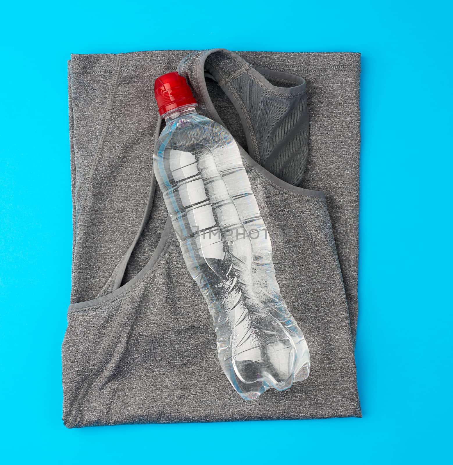 folded gray sports female T-shirt and water bottle on a blue background, concept of exercising water during fitness