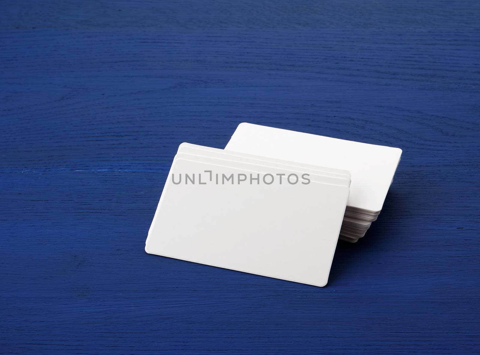 stack of white blank paper rectangular business cards on blue wooden background, template for designer
