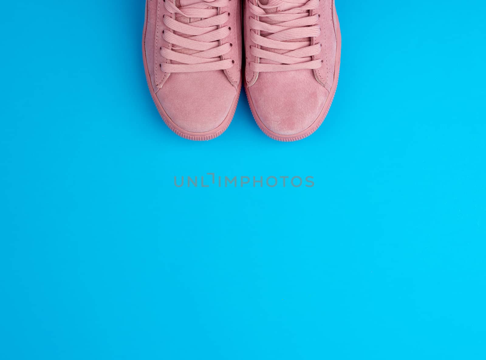 pair of sports pink sneakers with laces on a blue background, top view, place for text 