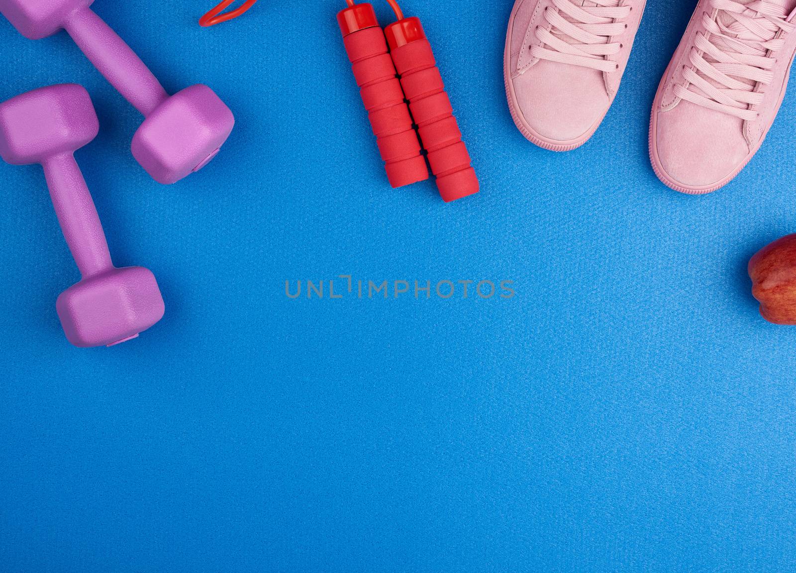 pair of pink suede sneakers, dumbbells and a red jump rope on a blue background, top view, set for sports, copy space