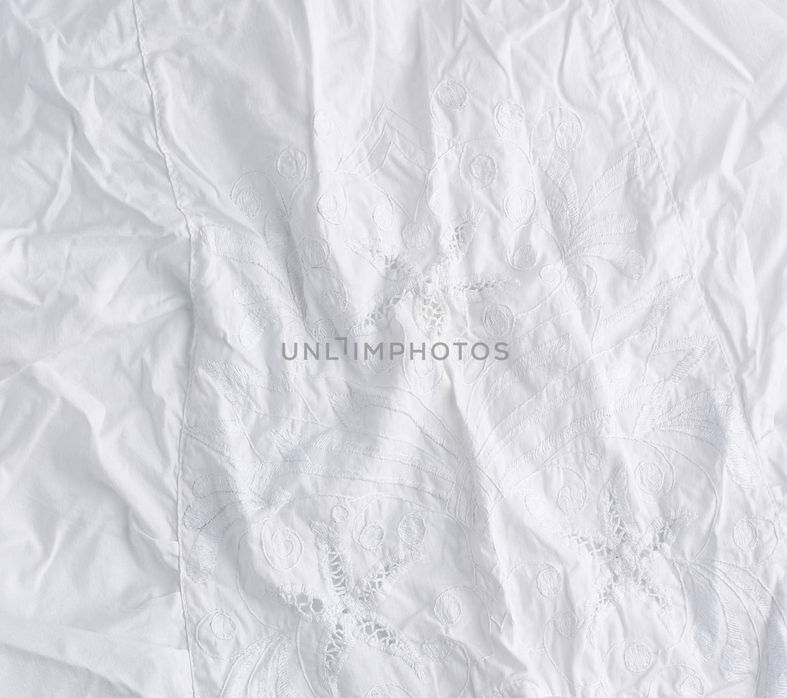 crumpled white cotton fabric with embroidery elements, fabric for sewing clothes and shirts, full frame