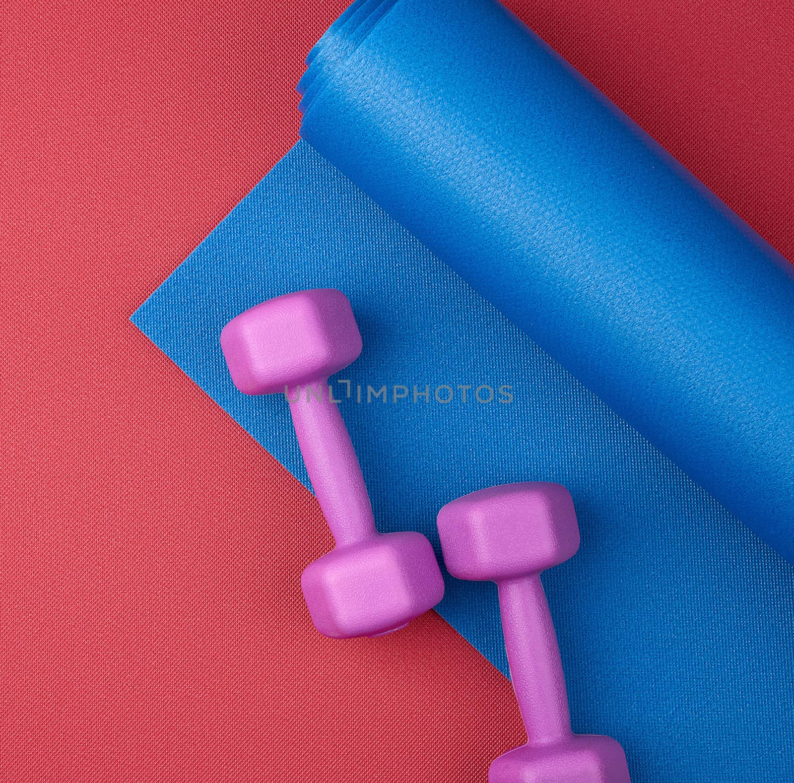 pair of purple plastic dumbbells on a blue neoprene mat, top view, training equipment