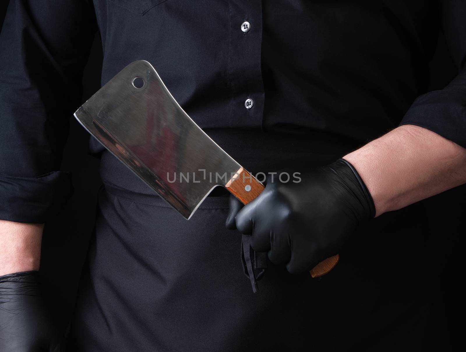 male cook in black uniform and black latex gloves holds a large sharp meat knife, close up