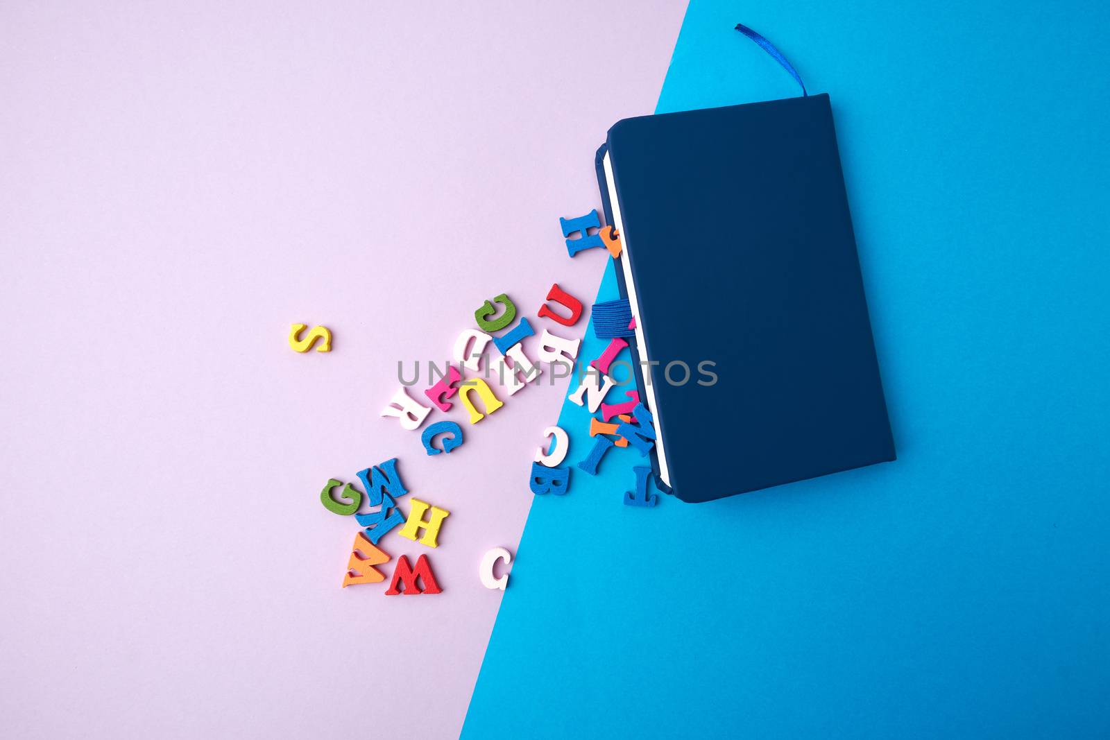blue notebook and scattered wooden multi-colored letters on an abstract background, top view, flat lay