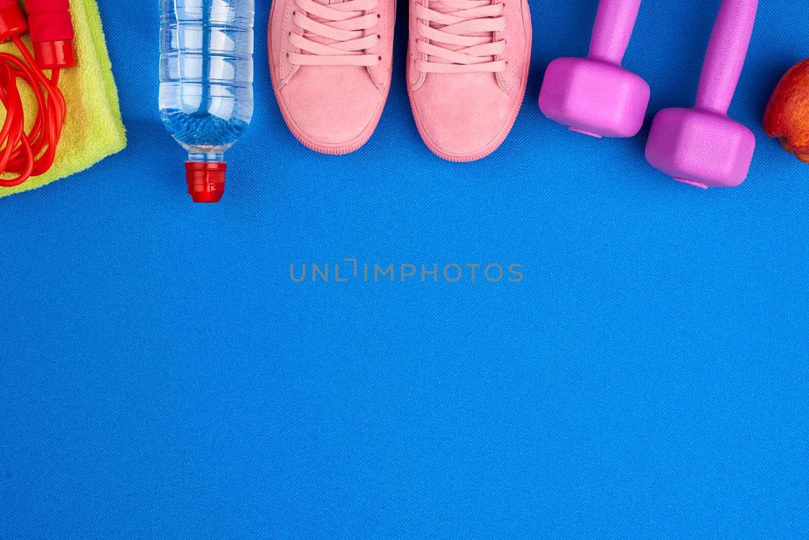 plastic purple dumbbells, sportswear, water, pink sneakers on a blue background from a sports mat, fitness kit, flat lay, copy space