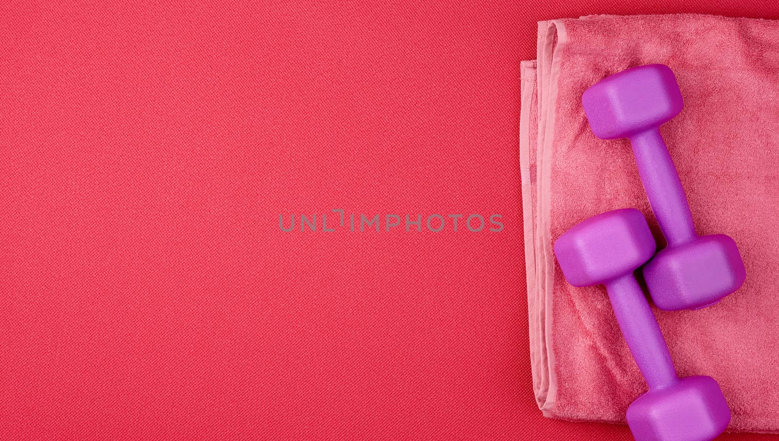 pair of purple plastic dumbbells and pink terry towel on a red neoprene mat, top view, training equipment, copy space
