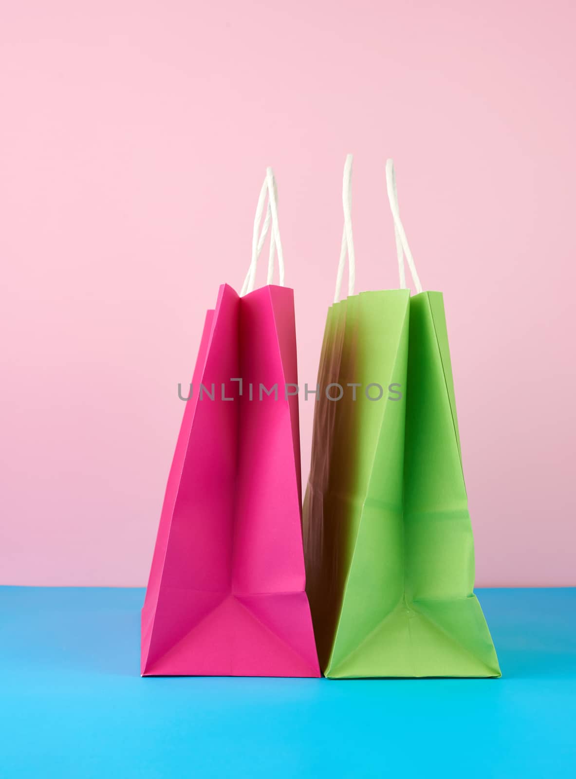empty multicolored paper bags for shopping and gifts with white handles stand on a pink-blue background